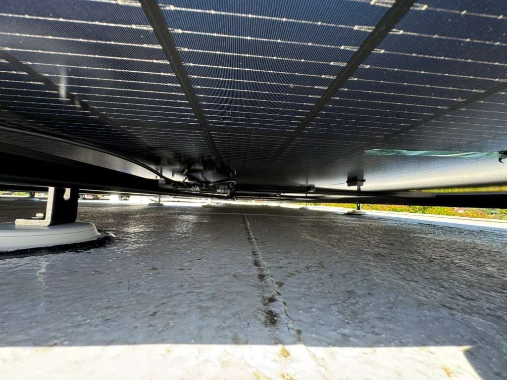 Underside detail of tilt-racked solar modules on a Belmont low-slope roof, showing clean wire management and rail work below the array.