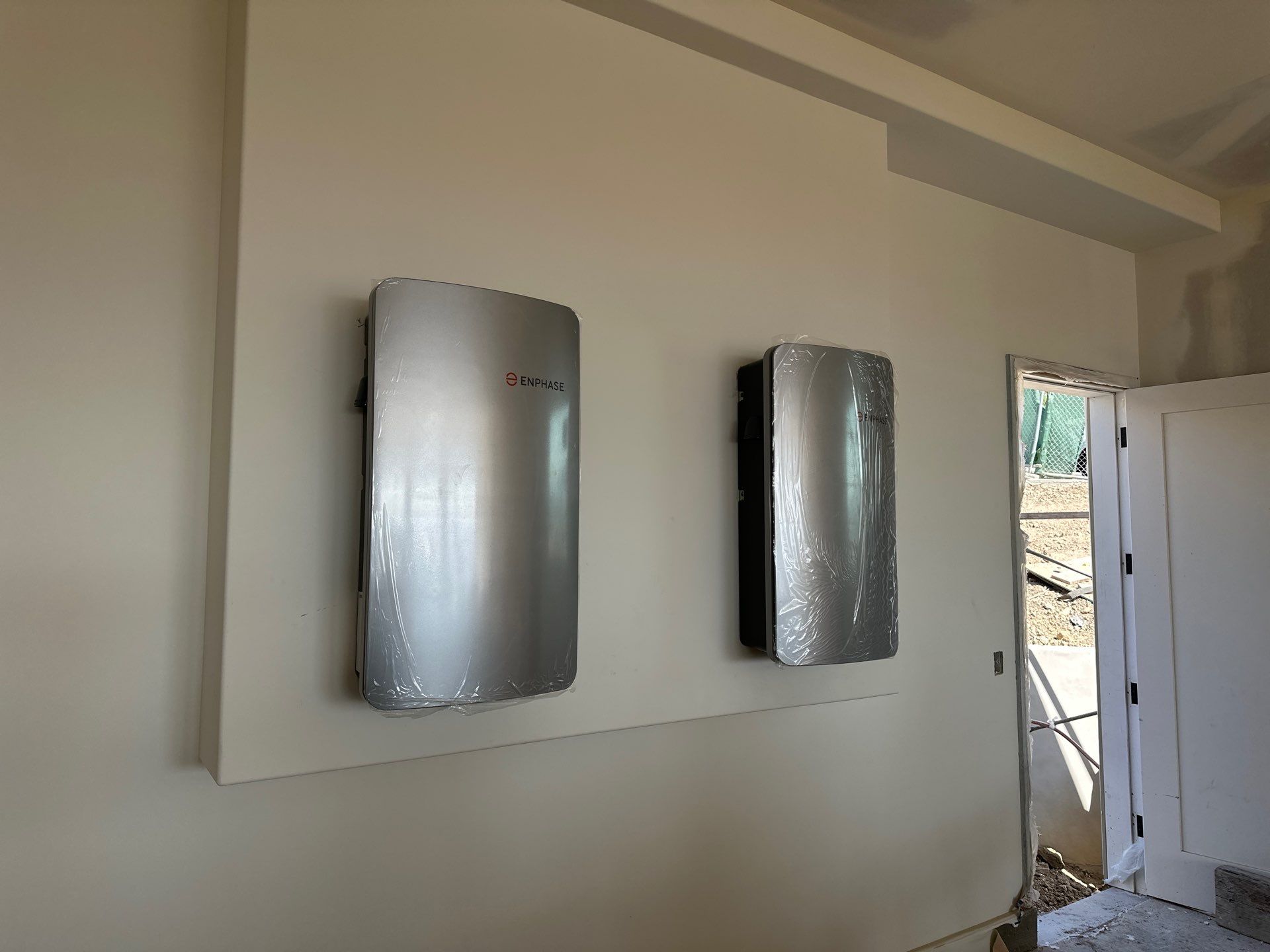 Two Enphase IQ solar inverter units surface-mounted on a clean interior garage wall of a Fremont home during final electrical commissioning.