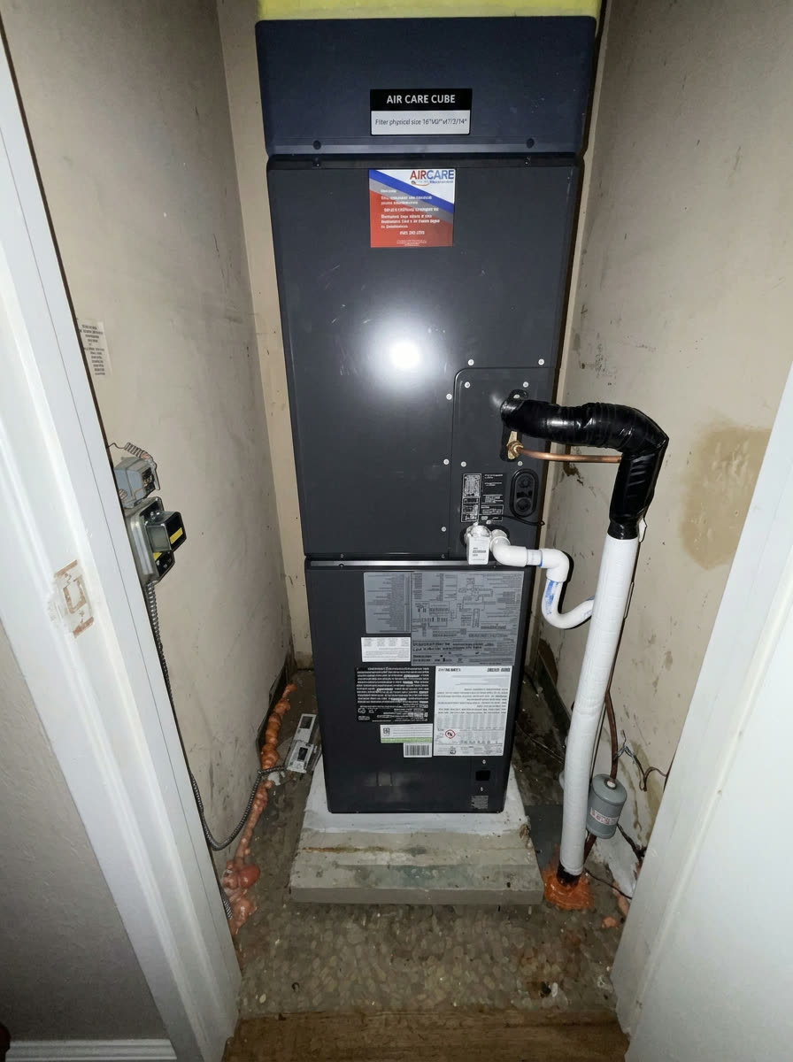 Air Care Cube high-efficiency air handler installed in a narrow interior utility closet with insulated line set and PVC condensate drain.