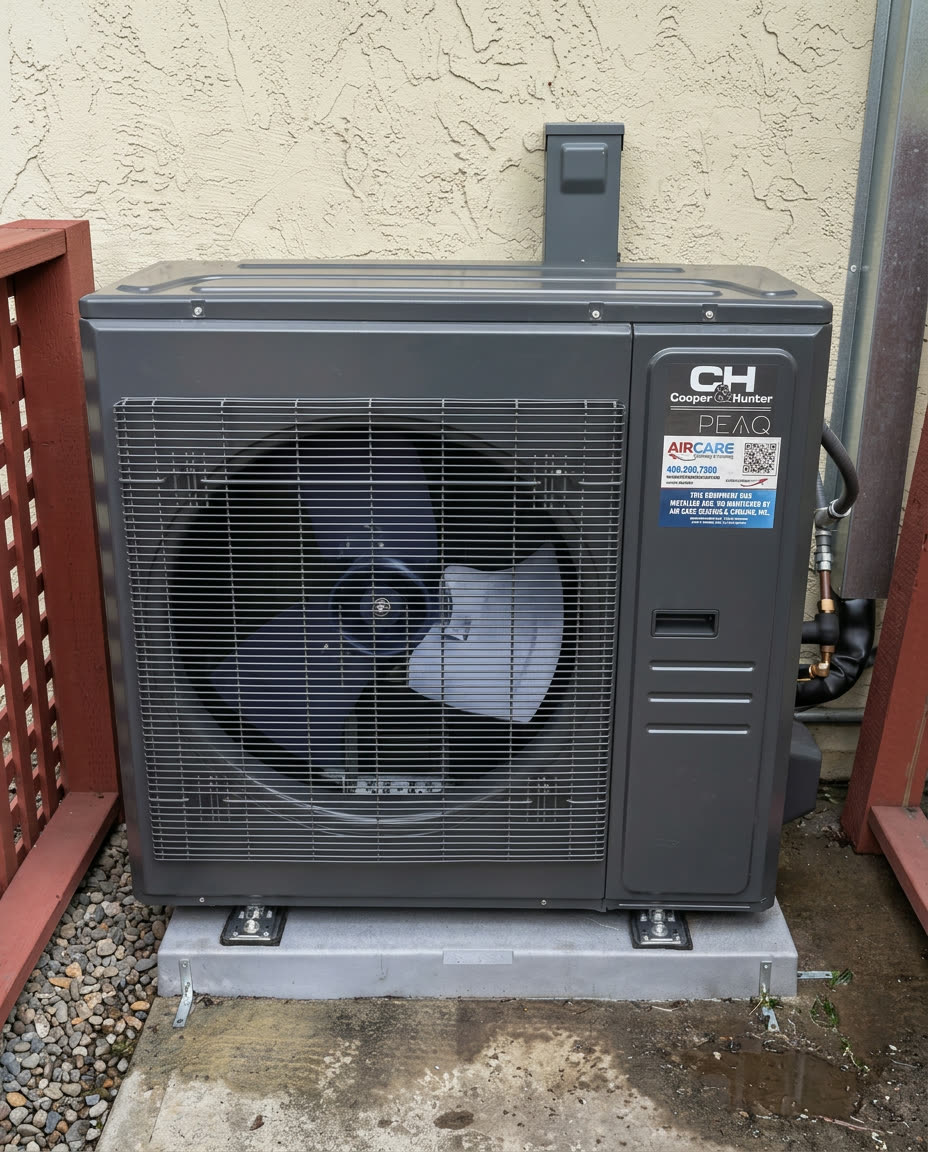 Dark gray Cooper & Hunter PEAQ side-discharge heat pump on a concrete pad against a beige stucco wall, tagged with an Air Care install sticker.