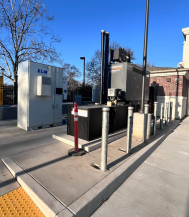 ELM lithium battery energy storage cabinet paired with a Generac inverter and disconnect gear on a concrete pad behind bollards at a Morgan Hill, CA commercial site.