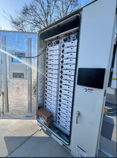 Interior of an ELM battery storage cabinet with the door open, showing racked lithium battery modules, monitoring display, and internal wiring at a Morgan Hill, CA commercial site.