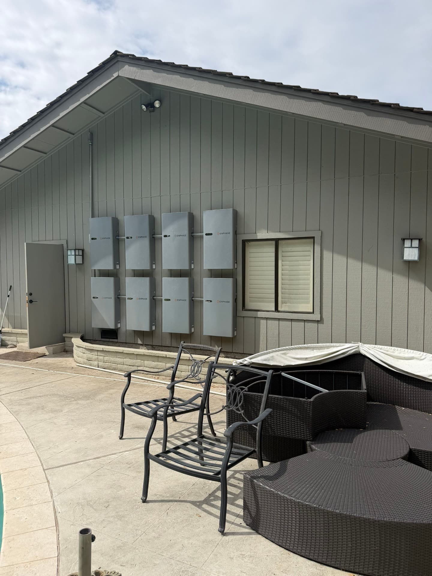 Two-by-four grid of Enphase IQ Batteries mounted on the gable-end wall of a Morgan Hill home, viewed from the patio.