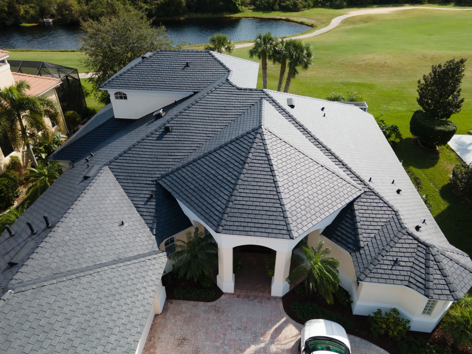 Aerial view of a luxury estate with a designer slate-profile composite roof in charcoal, overlooking a lake and golf course.