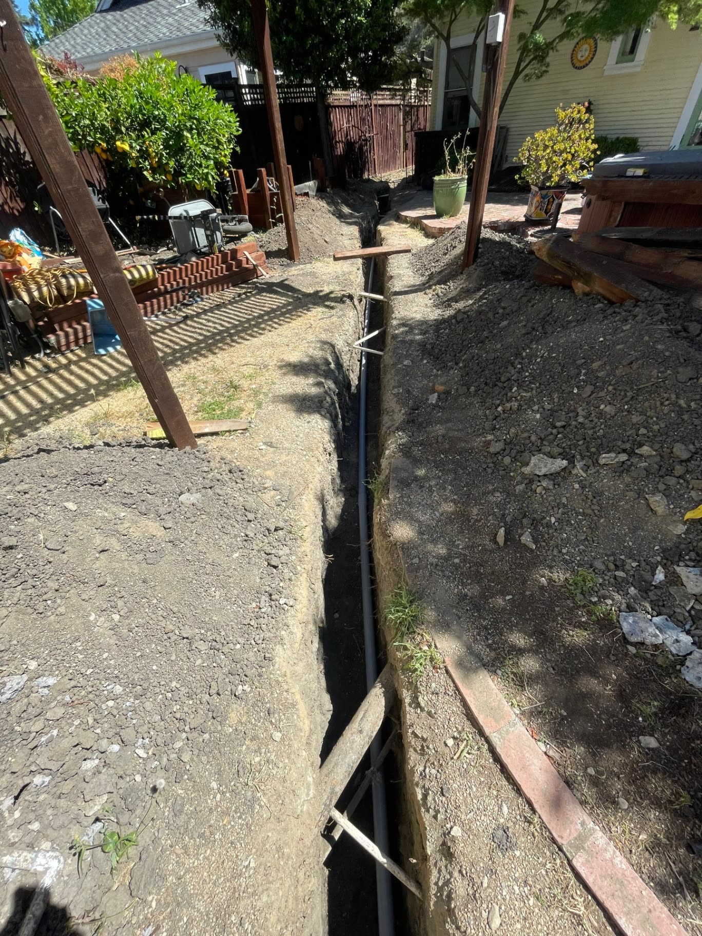 Deep, hand-dug conduit trench running between a Santa Clara home and detached structure, with electrical conduit laid at grade before backfill.