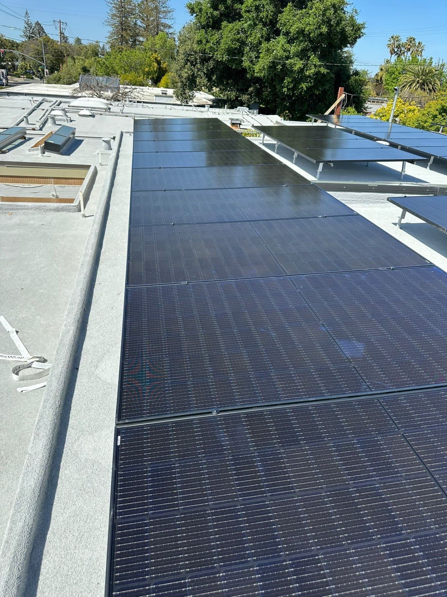 Long row of newly installed all-black solar modules along the edge of a low-slope Sunnyvale roof.