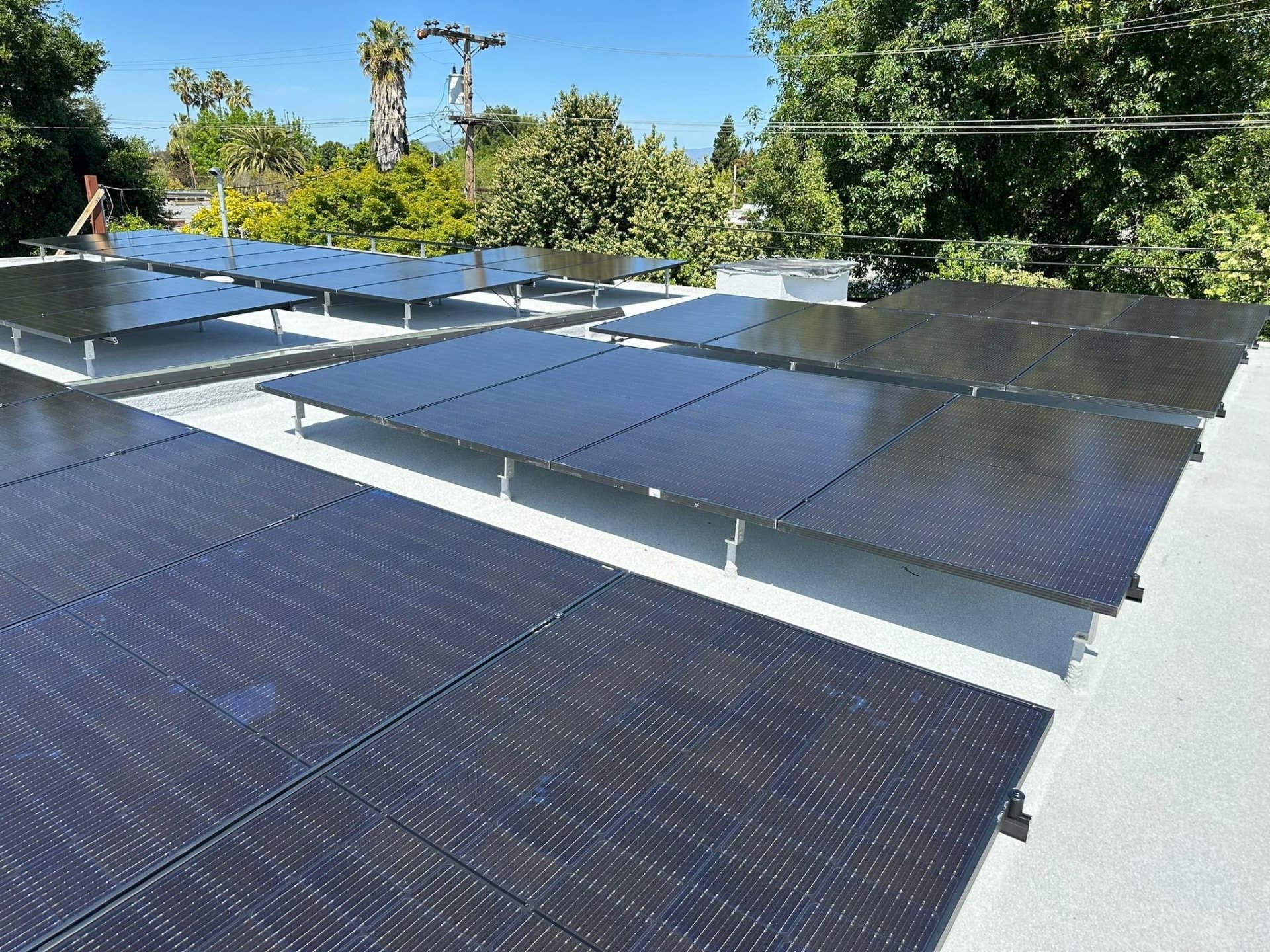 All-black low-slope rooftop solar array on a Sunnyvale home, tilt-racked panels facing south over a tree-lined neighborhood.