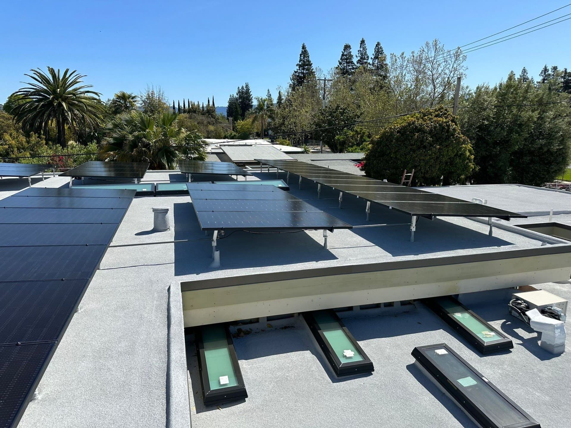 Multi-section rooftop solar array with tilt racking over a Sunnyvale flat roof, palm trees and hills in the distance.