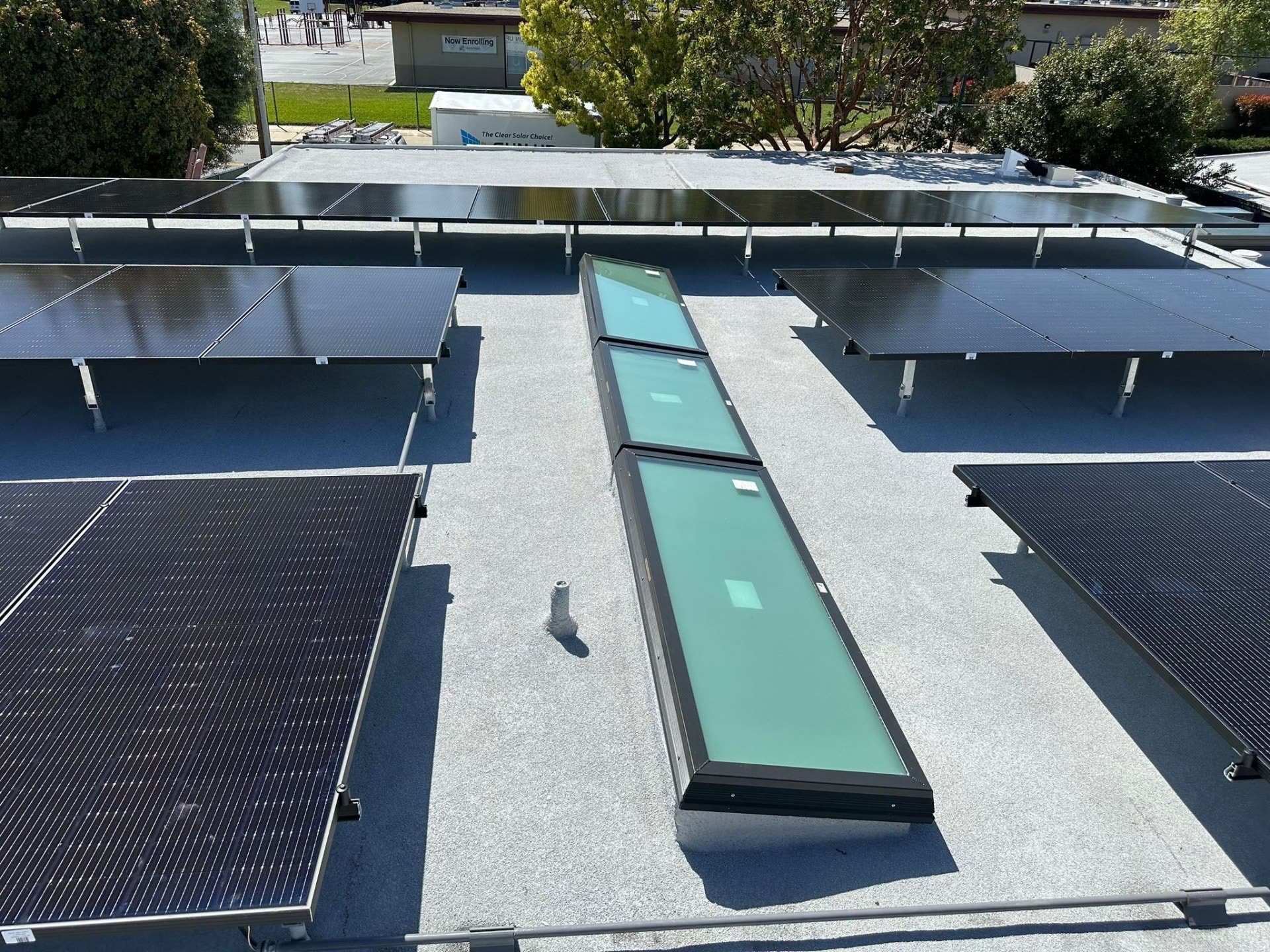 Tilt-racked solar panels arranged around a run of skylights on a low-slope Sunnyvale roof.